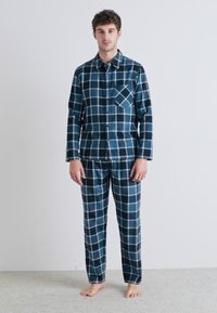 Ensemble de pyjama en flanelle à carreaux bleus, comprenant une chemise à boutons avec poche poitrine et un pantalon assorti, texture douce et coupe décontractée.