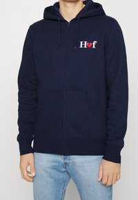 Námořnická modrá mikina na zip z bavlny, s kapsou vpředu, nastavitelnou kapucí a vyšívaným logem "H♥f" na hrudníku.