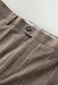 Braune Hose aus strukturiertem Stoff mit einem einzelnen Knopfverschluss und dezentem Webmuster. Flache Front mit innenliegendem Futterdetail.