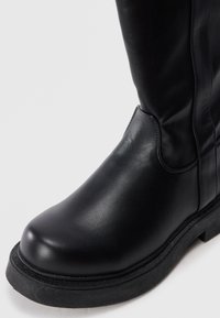 Black leather ankle boot with smooth texture, rounded toe, and prominent rubber sole. Side stitching visible along the upper.