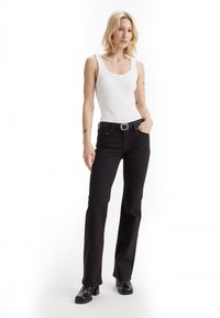 Black flared jeans with a slight stretch, high waist, five pockets, and a smooth texture. Paired with a fitted white tank top and black boots.
