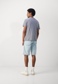Gestreepte marineblauwe en witte t-shirt, korte mouwen, gecombineerd met lichtblauwe denim shorts en witte sneakers. Het design heeft een klassieke pasvorm.