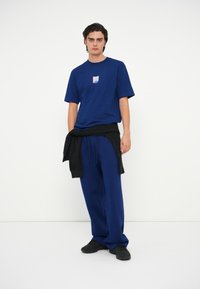 Donkerblauwe T-shirt met korte mouwen en een logopatch op de borst, gecombineerd met donkerblauwe sweatpants en zwarte sneakers.