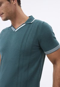 Teal puuvillane polo särk V-kaelusega, valgete triipudega krae ja dekoratiivsed õmblusread eesmises osas. Lühikesed varrukad triibuliste aktsentidega.