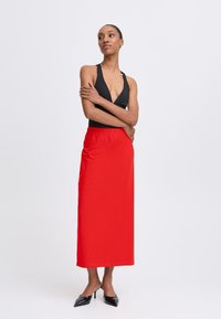 Melna halter top un gara sarkana svārku ar elastīgu jostu, kas piedāvā elegantu siluetu un augstus papēžus. Gluda auduma tekstūra.