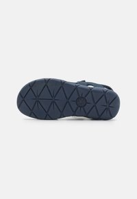 Suela de sandalia de goma en color navy con una superficie texturizada que presenta patrones en forma de diamante para mayor tracción. Correas visibles para el soporte del pie.
