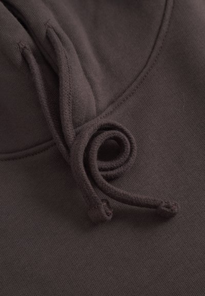 Gros plan sur le tissu d'un hoodie brun foncé montrant la couture ainsi que les deux extrémités de cordon tournées en boucle.
