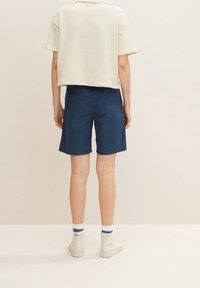 Jasno-beżowy, krótki t-shirt i granatowe szorty; materiał bawełniany; połączone z białymi botkami za kostkę i paskowanymi skarpetkami, widok z tyłu.