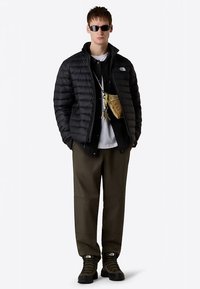 Černá prošívaná bunda, černá košile na zapínání na knoflíky, bílé tričko, olivové kalhoty a černé boty. Malá zlatá kabelka přes rameno a tmavé sluneční brýle.