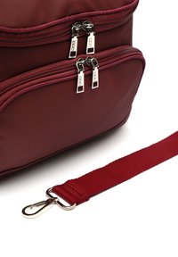 Bolsa de nylon roja con dos compartimentos con cremallera, herrajes plateados y una correa de tela desmontable. Textura suave con un acabado mate.