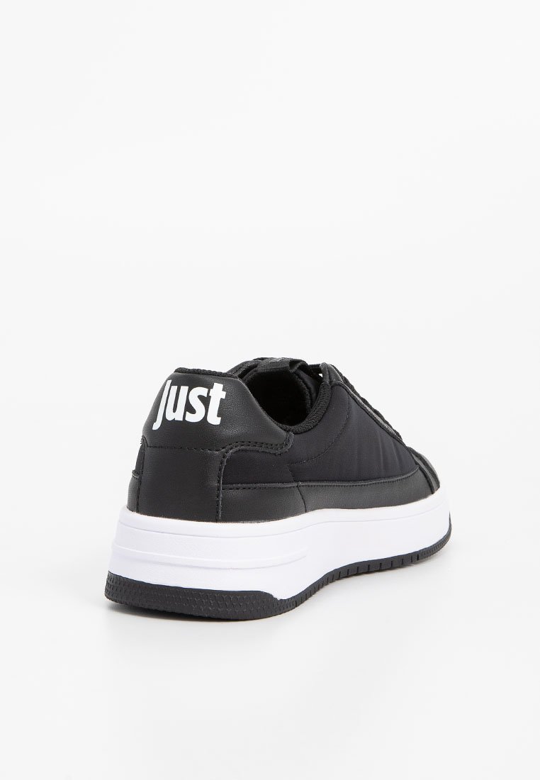 Czarny sneaker z gładką syntetyczną cholewką, białą podeszwą i kontrastowym białym napisem "Just" na pięcie. Zaokrąglony kształt i teksturowana podeszwa.