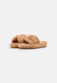 Fuzzy tan slide slippers with two cross straps, featuring a metallic square buckle. Textured outsole provides grip and comfort.