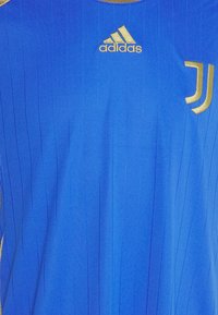 Camiseta atlética azul con rayas verticales, que presenta el logo dorado de Adidas y el emblema de la Juventus en el lado izquierdo. Tela ligera y texturizada.