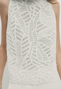 Haut dos nu blanc avec un motif en dentelle complexe présentant des motifs géométriques et floraux sur la partie supérieure du corps d'une personne.