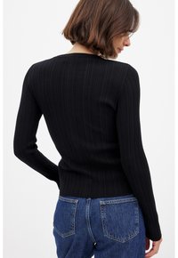 Svart ribbade långärmad topp med rund halsringning, slim fit och texturerad tyg. Matchas med högmidjade blå denimjeans.