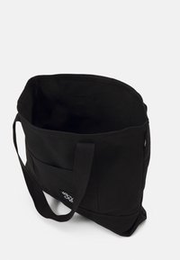 Svart canvas tote-väska med två hållbara handtag, ett rymligt inre och en framficka. Har en enkel design med minimal detaljering.