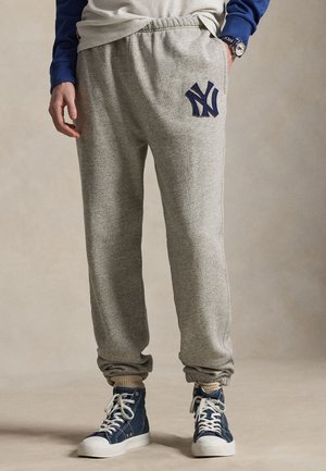Person iført grå joggingbukser med navy-logo, blå høje sneakers, beige sokker og en delvist synlig blå langærmet skjorte.