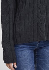 Black knitted sweater with ribbed and cable-knit patterns, featuring a relaxed fit and long sleeves, paired with denim jeans.