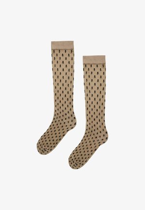 Beige knielange transparente Socken mit schwarzen Blattmustern und festen beigen Bündchen oben.
