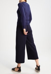 Tmavě modrý přiléhavý svetr, krátké široké kalhoty a černé espadrilky. Hladká pletená textura a jednoduchý, čistý design bez viditelných vzorů.