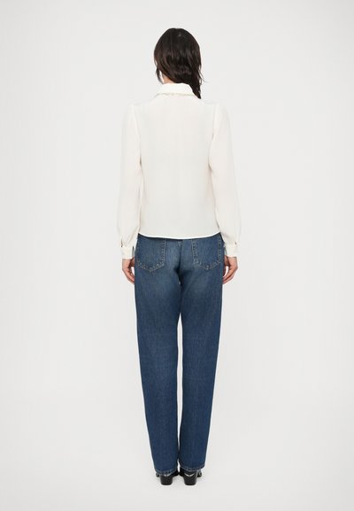 Λευκό πουκάμισο με μακριά μανίκια και γιακά, συνδυασμένο με μπλε τζιν ψηλόμεσο. Το πουκάμισο έχει ομαλή υφή, ενώ το τζιν έχει άνετη εφαρμογή.