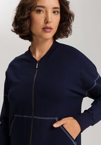 Marine blauwe zip-up jas van zachte stof, met een staande kraag, twee voorzakken en contrasterende stiksels langs de naden en randen.