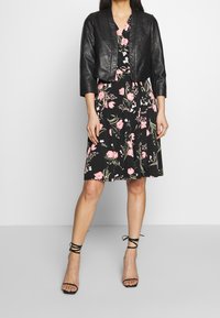 Černá kožená zkrácená bunda přes květinové šaty ke kolenům s růžovými a zelenými vzory. Obsahuje černé lodičky se sponou na kotníku.