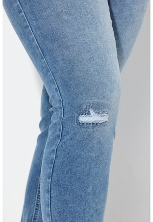 Hellblaue Denim-Jeans mit einer figurbetonten Passform, die ein beschädigtes Knie mit ausgefransten Kanten und subtiler Textur aufweisen.
