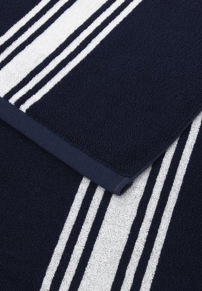 Serviette bleu foncé avec trois rayures blanches parallèles, une pliée, montrant un tissu en coton texturé.