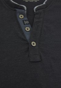 Tmavě šedé henley tričko s knoflíkovou légou zaoblenými knoflíky, kontrastním podšitím límce a textilním štítkem na levé straně.