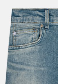 Lichtblauwe spijkerbroek van denim met een vervaagd textuur, voorzien van een klein voorvak, oranje stiksels en een ronde metalen knop.