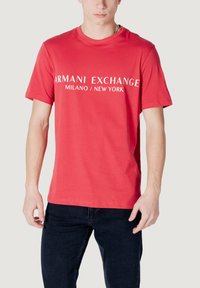 T-shirt in cotone rosso con maniche corte e scollatura a girocollo, con la scritta bianca "ARMANI EXCHANGE MILANO / NEW YORK" in evidenza.