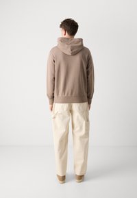 Bruine katoen hoodie met een trekkoord capuchon, gecombineerd met off-white cargobroek met zakken. De outfit omvat bruine suède schoenen.