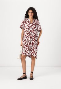 Robe à manches courtes, couleur bordeaux avec des motifs de feuilles blanches, dotée d'un col à boutons et d'échancrures latérales, associée à des ballerines noires à lacets.