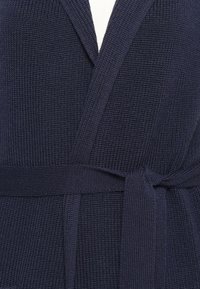 Mornarska pletena cardigan jakna s teksturiranim materijalom, otvorenim prednjim dijelom i samovezicom u struku. Materijal ima mekani, tkaninski izgled.