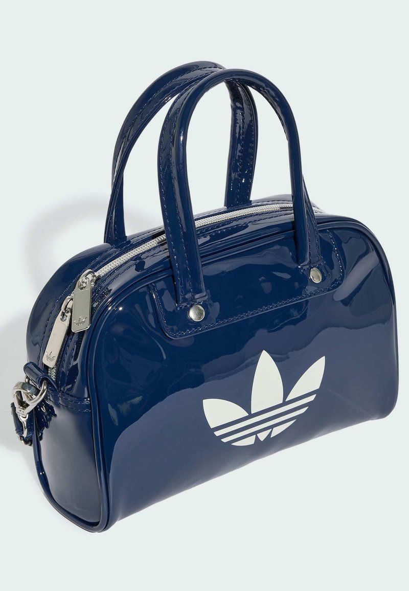 Glänzende dunkelblaue Handtasche mit zwei Griffen, silbernen Reißverschlüssen und einem großen weißen Adidas-Trefoil-Logo auf der Vorderseite.