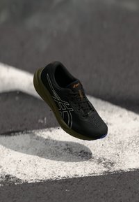 Black athletic shoe with breathable upper, rubber sole, and raised accents. Features a sleek design with a textured surface and reflective details.