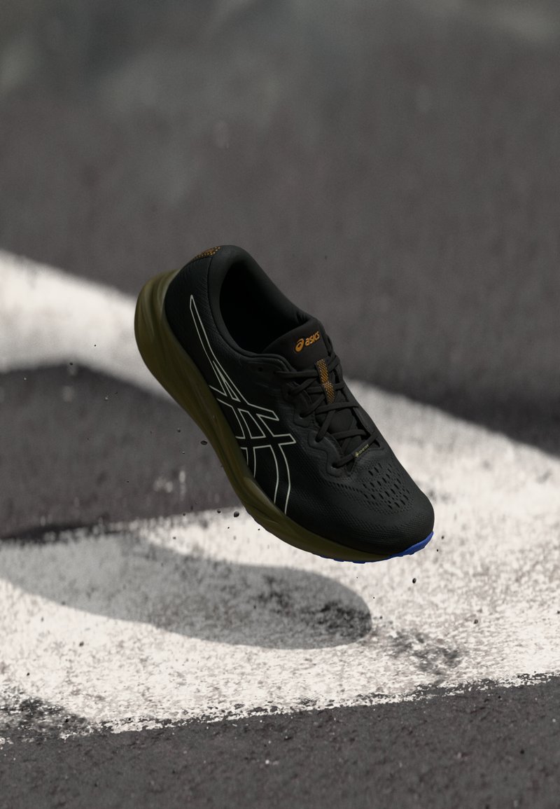 Black athletic shoe with breathable upper, rubber sole, and raised accents. Features a sleek design with a textured surface and reflective details.
