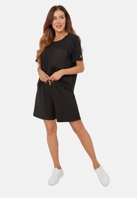 Czarna koszulka z kieszonką na piersi, zestawiona z czarnymi szortami z elastycznym pasem i sznurkiem. Model nosi białe sneakersy.