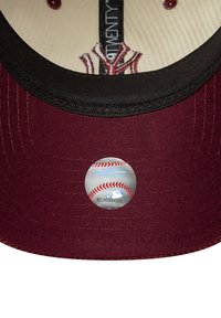 Bordo bejzbol kapa s crnim vizirima, slična srebrnoj MLB oznaci na dnu. Unutrašnjost ima bež podstavu s izvezenim detaljima.