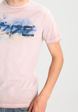 Lys pink bomulds T-shirt med et blåt og gult grafisk design med fed skrift. Rund hals, korte ærmer og en blød tekstur.
