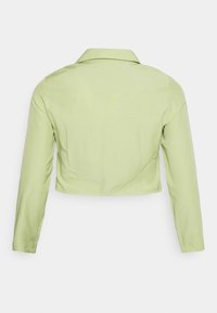 Casaco cropped em tecido verde claro, com mangas compridas e colarinho. Textura suave com um design simples, sem padrões ou acessórios visíveis.