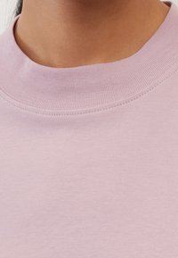 Light pink crew-neck sweatshirt with a textured finish and ribbed collar. Features a smooth fabric and precise stitching along the edges.