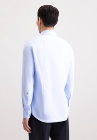 Camicia azzurra a maniche lunghe con una texture liscia, polsini con bottoni e orlo curvo. La vista posteriore mostra un colletto classico e una vestibilità su misura.