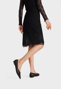 Ballerine nere con punta affilata, con tomaia in rete e dettagli lucidi, e un tacco basso a blocco, ideali per occasioni eleganti.