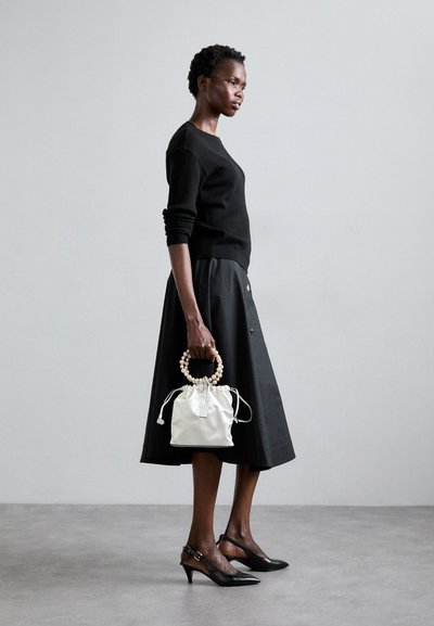 Black ribbed sweater, black skirt with buttons, white drawstring handbag with a beaded handle, black high-heeled shoes, matte background.