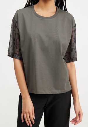 T-shirt vert olive à manches courtes avec des accents en transparence de motif léopard. Texture lisse avec une coupe décontractée.