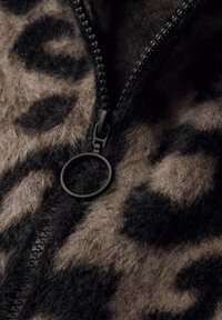 Brązowa i czarna tkanina w cętki lamparta o miękkiej, puszystej fakturze, z czarnym zamkiem błyskawicznym i okrągłym czarnym uchwytem.