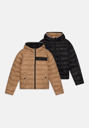 Vestes matelassées réversibles en marron et noir, avec un design matelassé, fermeture éclair à l'avant, capuche et accent logo sur la poche poitrine.