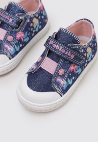 Zapatillas de denim azul con un acabado brillante, que cuentan con una correa de Velcro rosa, patrones de sirenas y estrellas coloridas, y suelas de goma blancas.